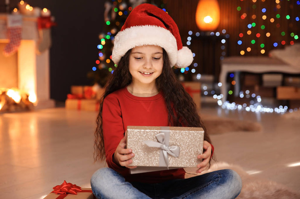 Cute little child in Santa hat with Christmas gift box at home - Фото, изображение