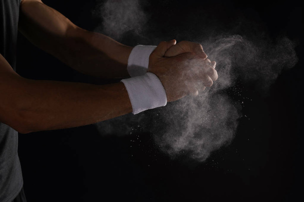 Young man applying chalk powder on hands against dark background - Photo, Image