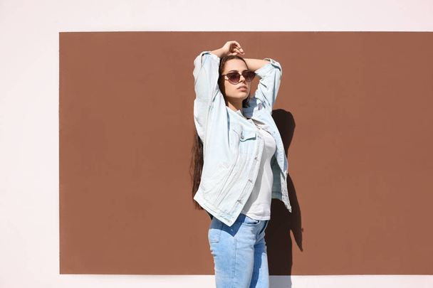 Young hipster woman in stylish jeans and jacket posing near color wall - 写真・画像