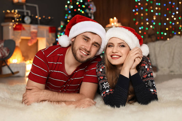 Happy young couple in Santa hats celebrating Christmas at home - Foto, Imagen