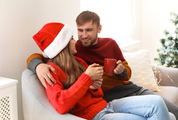Happy young couple with cups of hot drink celebrating Christmas at home - Valokuva, kuva