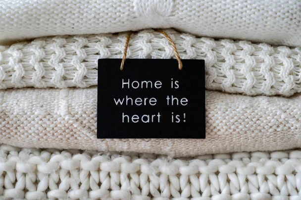 inscription HOME IS WHERE THE HEART IS Background with warm sweaters. Pile of knitted clothes in warm shades, space for text, Autumn winter concept. Copy Space. - Фото, изображение