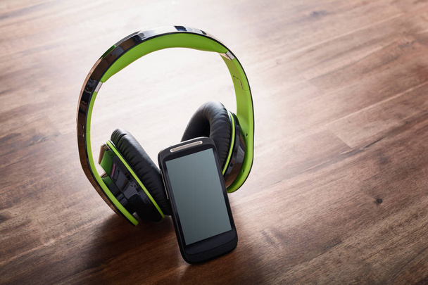 Bezdrátové poslouchat hudební koncept s Smartphone, opírající se o velké černé režijní sluchátka na dřevěný stůl - Fotografie, Obrázek