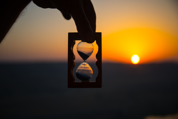 生活時間渡すことの概念。夕焼け空の背景を持つ砂時計を持っている手。選択と集中 - 写真・画像