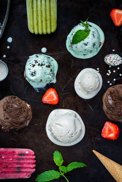 Выбор различных шариков мороженого, таких как мята, шоколад и клубника на темном фоне, вид сверху
 - Фото, изображение