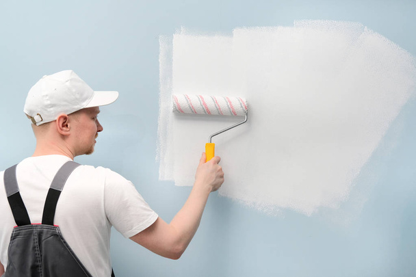 Человек, работающий в белой футболке и кепке, рисует стену
. - Фото, изображение