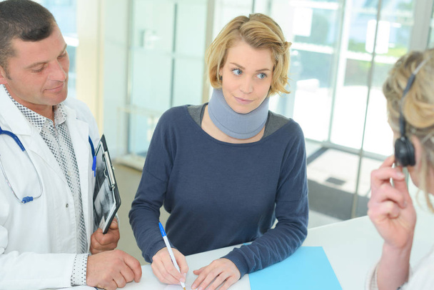 female patient with cervical collar in clinic signing document - Photo, Image
