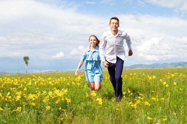 Para młodych ludzi biegają pola z kwiatami - Zdjęcie, obraz