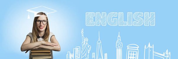 Ein junges Mädchen in weißem Kleid und Brille legt ihre Hände auf einen Stapel Bücher auf blauem Hintergrund. Hinzufügen des Textes in Englisch. Konzept des Englischlernens. Ikonen mit Attraktionen von London und New York. - Foto, Bild