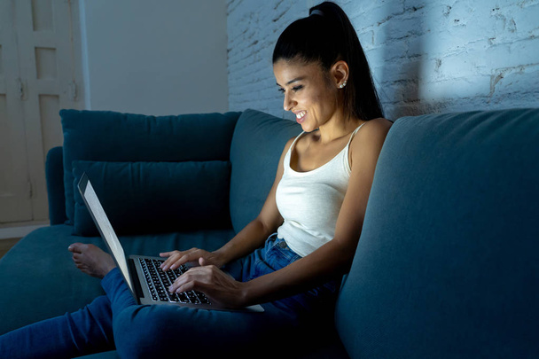 young attractive hispanic and relaxed woman at home smiling happy on sofa couch using laptop computer in dark evening light enjoying watching online movie or addicted to internet social network. - Fotoğraf, Görsel