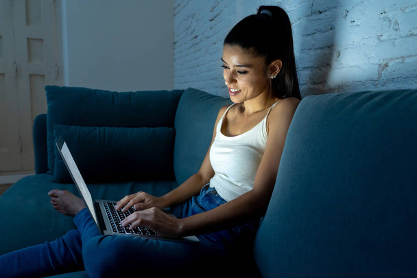 young attractive hispanic and relaxed woman at home smiling happy on sofa couch using laptop computer in dark evening light enjoying watching online movie or addicted to internet social network. - Foto, Bild
