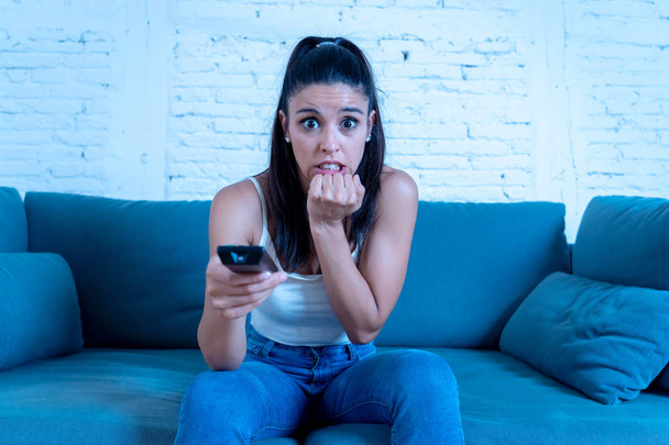 young beautiful latin woman sitting at home sofa couch in living room watching television scary horror movie or horrible news scared and excited covering her eyes holding remote control. - Photo, image