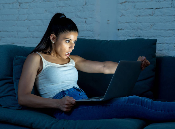 young beautiful hispanic internet addict woman in casual clothes sitting on the couch working bored and tired with laptop computer late at night in dark room light exhausted from work. - Foto, immagini