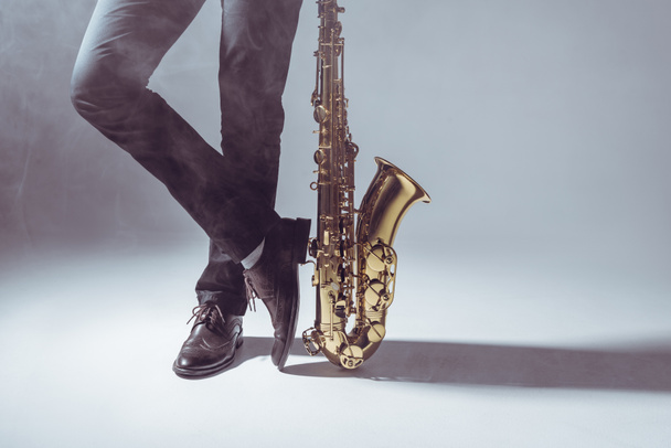 Unterteil des Berufsmusikers steht mit Saxophon in Rauch auf grau  - Foto, Bild