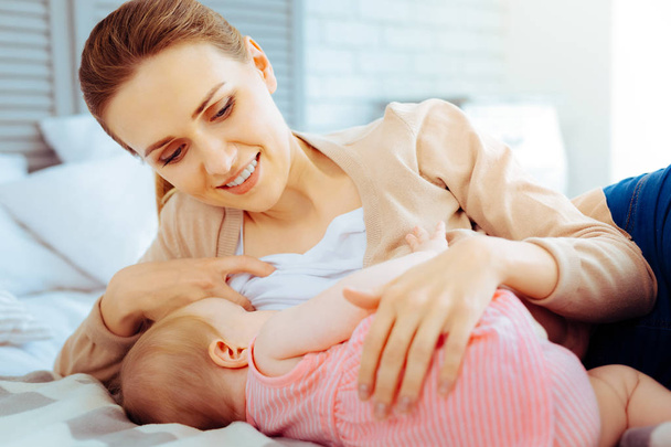Breast feeding. Beautiful young woman keeping smile on her face while giving breast to her kid - Фото, зображення