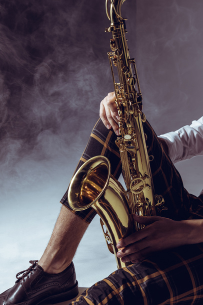 recortado disparo de elegante músico sosteniendo saxofón en humo en gris
 - Foto, imagen