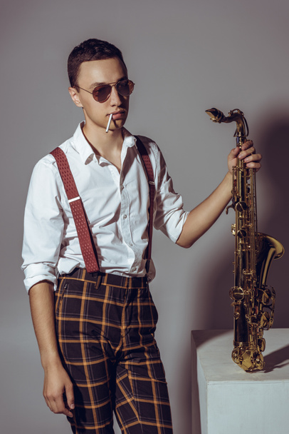 elegante joven músico con saxofón celebración de cigarrillos en gris
 - Foto, imagen