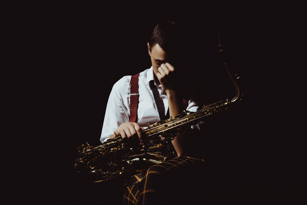 joven músico sosteniendo saxofón aislado en negro
  - Foto, Imagen