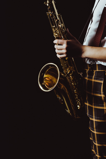 recortado disparo de elegante joven músico sosteniendo saxofón aislado en negro
 - Foto, imagen