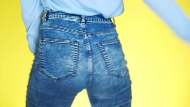 a girl in jeans with beautiful round buttocks is sexually moving. close-up. 4k, slow motion, colored yellow background - Materiał filmowy, wideo