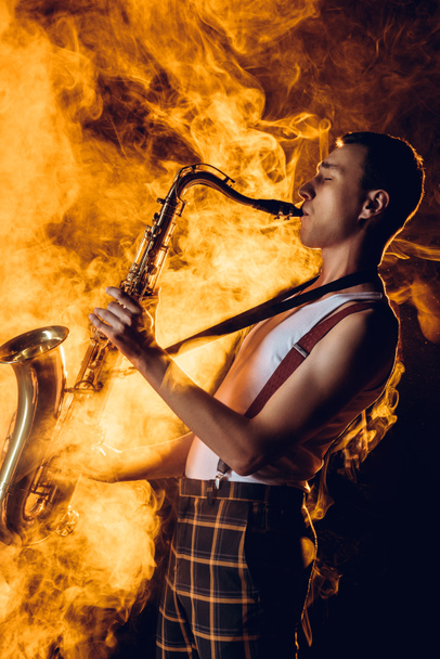 side view of stylish professional saxophonist playing sax in smoke  - Φωτογραφία, εικόνα