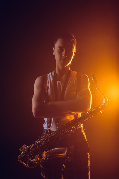 joven músico guapo con saxofón de pie con los brazos cruzados y mirando a la cámara
 - Foto, imagen