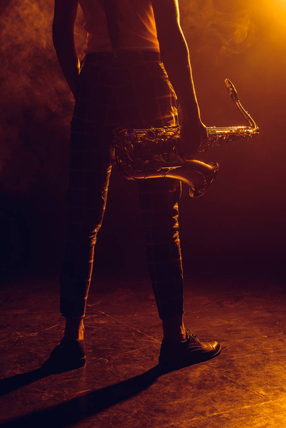 sección baja de joven músico sosteniendo saxofón en el escenario
  - Foto, imagen