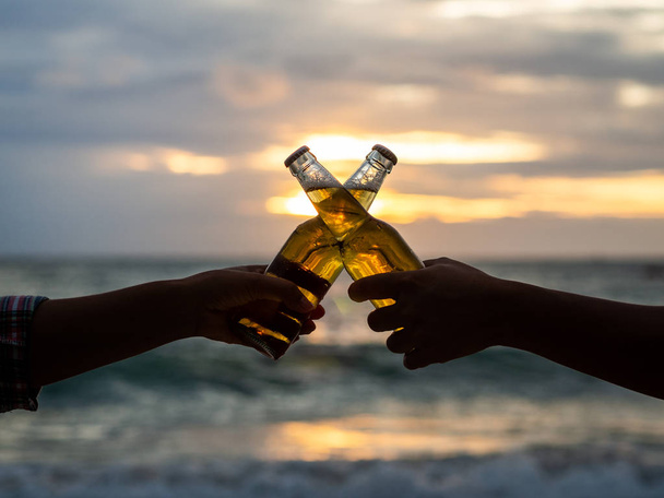 Couple hands holding beer bottles and clanging on the sunset beach. Party, Holiday, Summer, Friendship Concept. - Photo, Image