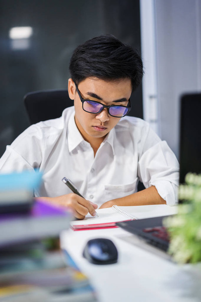 νεαρός άνδρας σπουδάζει και γράφει στο σημειωματάριο με φορητό υπολογιστή - Φωτογραφία, εικόνα