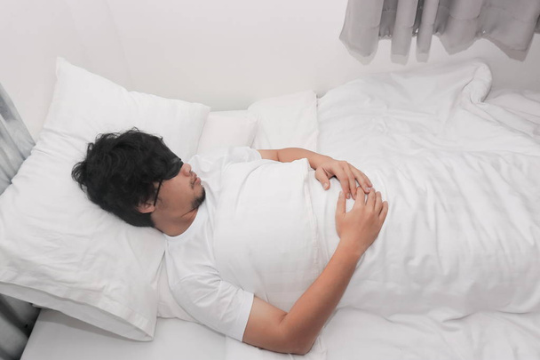 Mladý asijský muž se zavázanýma očima maska spí na bílé posteli v ložnici. - Fotografie, Obrázek