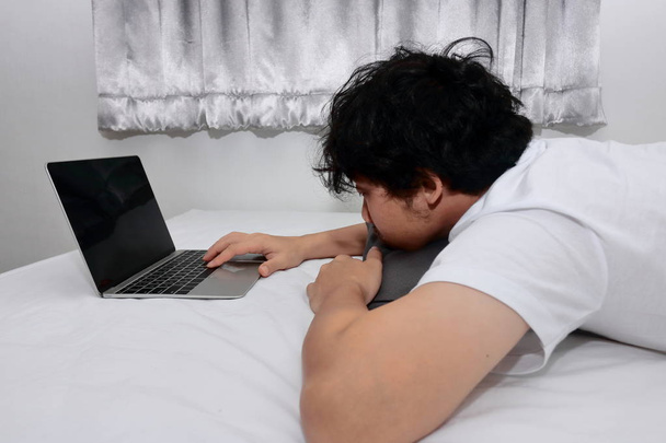 Young Asian man with laptop lying down on the bed in bedroom. - Foto, immagini