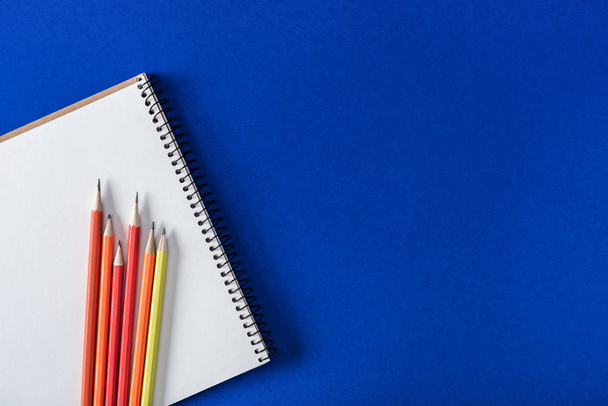 top view of various colorful pencils and blank textbook on blue background  - Foto, Bild