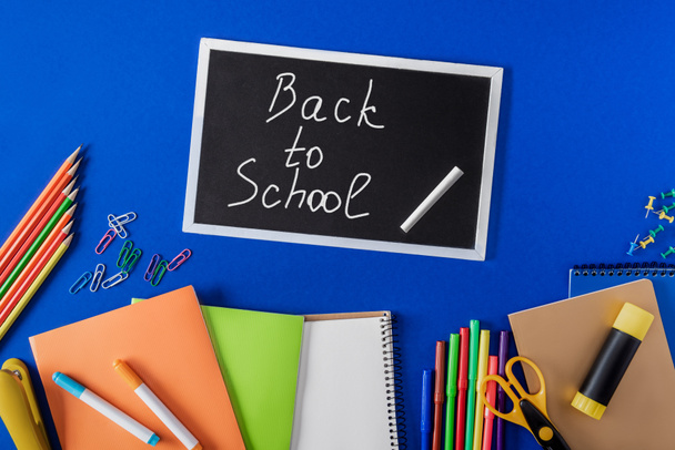 top view of chalkboard with lettering back to school and variety stationery on blue background  - Foto, Imagem