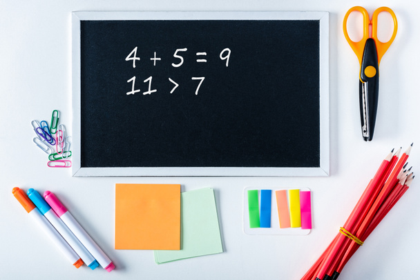 Ansicht der Tafel mit Mathe-Summen und verschiedenen Schulmaterialien auf weißem Hintergrund  - Foto, Bild