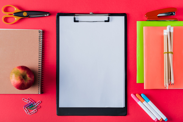top view of empty clipboard, apple and arranged variety stationery on red background  - Zdjęcie, obraz