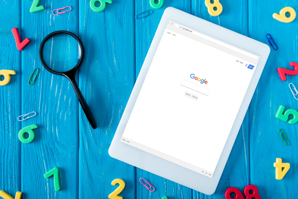 bovenaanzicht van digitale tablet met google website op scherm, Vergrootglas, paperclips en kleurrijke cijfers op blauwe houten achtergrond  - Foto, afbeelding