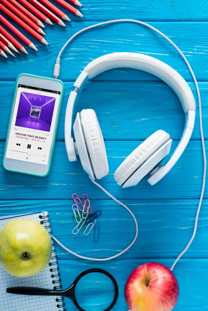 top view of smartphone with apple music application on screen, headphones, apples and stationery on blue wooden background  - Foto, Imagem