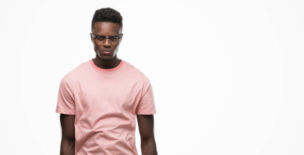 Jonge Afro-Amerikaanse man dragen van roze t-shirt met ernstige uitdrukking op het gezicht. Simpel en natuurlijk kijken naar de camera. - Foto, afbeelding