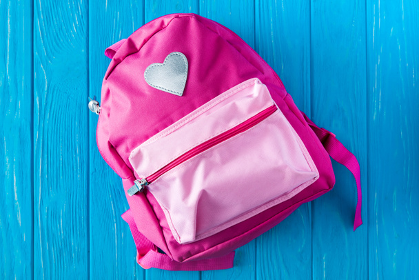 top view of pink backpack on blue wooden background - Fotó, kép