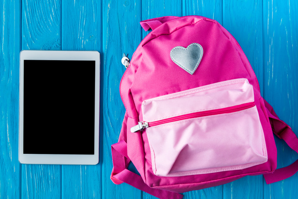 felülnézet, digitális tabletta, üres képernyő és a rózsaszín hátizsák, kék fa háttér  - Fotó, kép