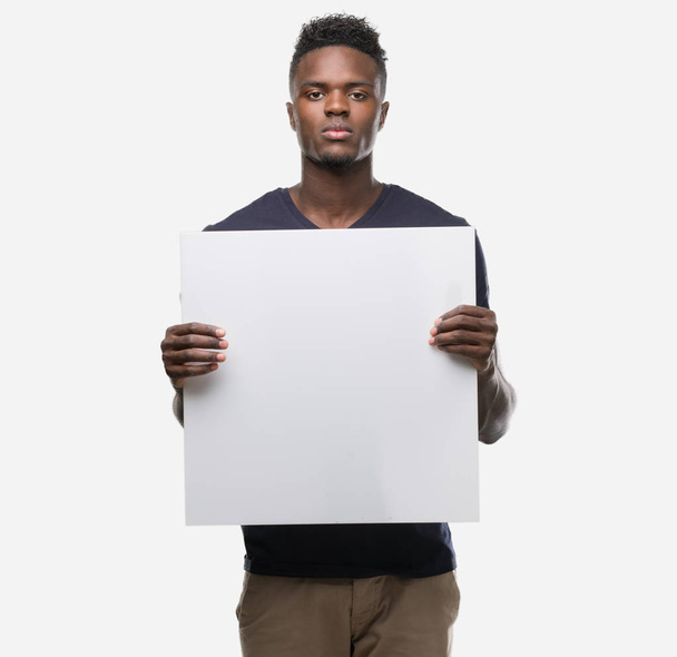 Fiatal afroamerikai férfi, kezében egy banner egy magabiztos kifejezés, a gondolkodás súlyos Szúró Szembenéz - Fotó, kép