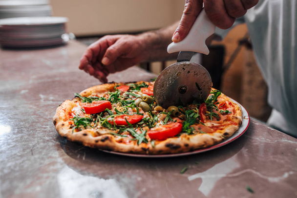 Close-up image of hand of chef baker cutting pizza. - Φωτογραφία, εικόνα