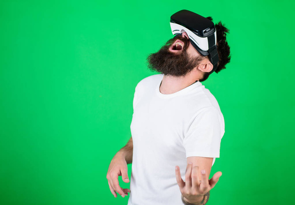 Guy with VR glasses learn to play music on guitar. VR musician concept. Man with beard in VR glasses, green background. Hipster guitarist on enthusiastic face use modern technology for entertainment. - Фото, изображение