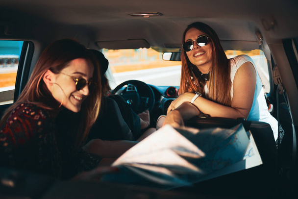 Deux jeunes femmes qui s'amusent sur la route en regardant la carte. Troisième fille au volant
. - Photo, image