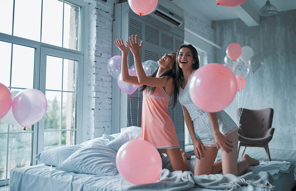 Dos mujeres atractivas jóvenes se divierten en casa en el dormitorio. Fiesta de pijamas para niñas
. - Foto, imagen