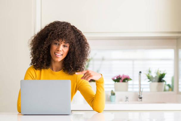 Африканская американка с помощью компьютера ноутбука на кухне очень счастлива указывая рукой и пальцем
 - Фото, изображение