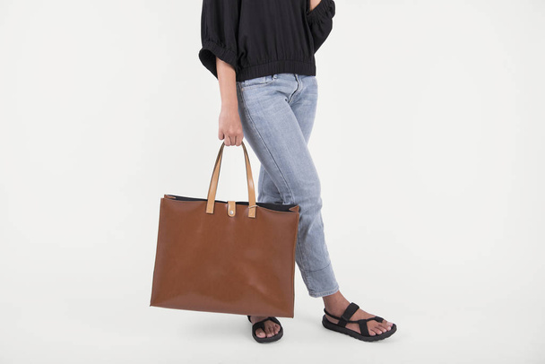Девушка держит коричневую кожаную сумку для макета пустой шаблон изолирован на сером фоне
.  - Фото, изображение