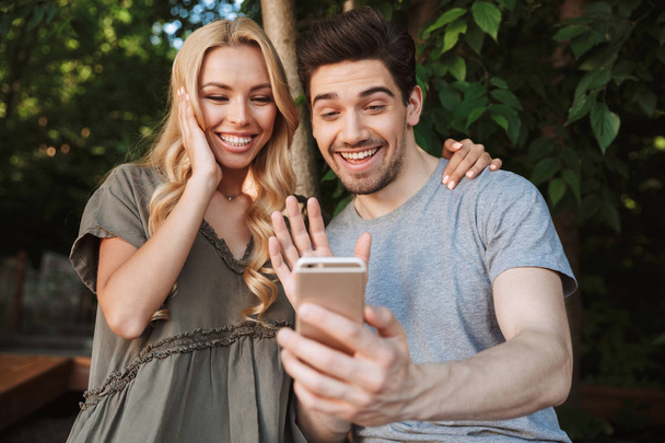 Excited young couple taking a selfie together while standing at a city park - Fotó, kép