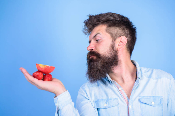 Man strict face with beard offers organic treats. I have treats for you. Man offers to try strawberries and apple fruit treats blue background. Hipster bearded holds strawberries and apple on palm - Foto, Bild