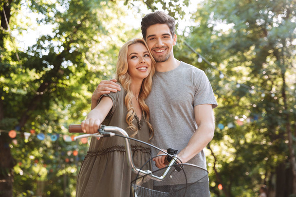 Pleased lovely young couple posing together with bicycle and looking at the camera outdoors - Φωτογραφία, εικόνα